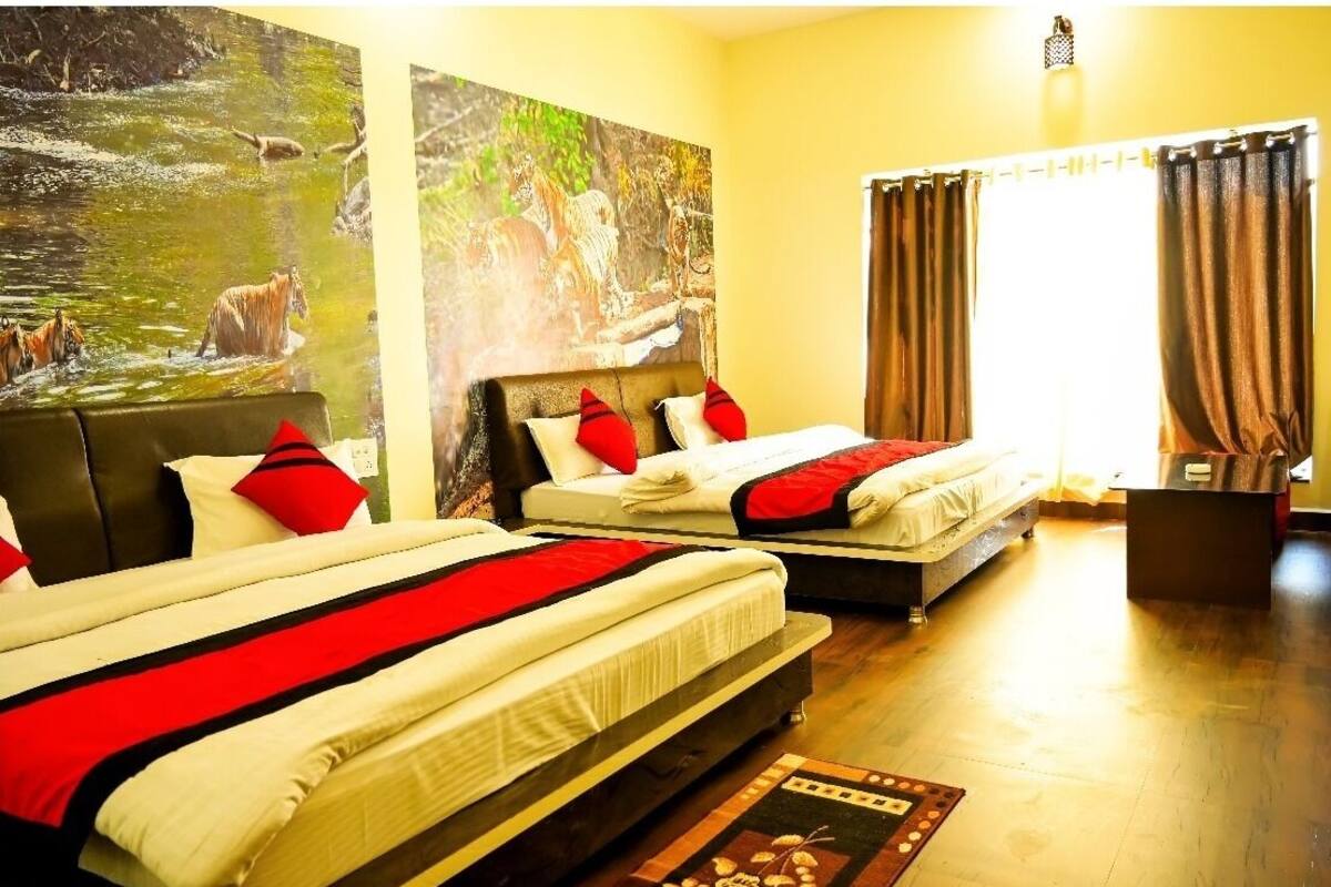 Habitación de hotel con dos camas, cada una con ropa de cama roja y blanca, un cuadro grande de un paisaje fluvial y una ventana con cortinas.