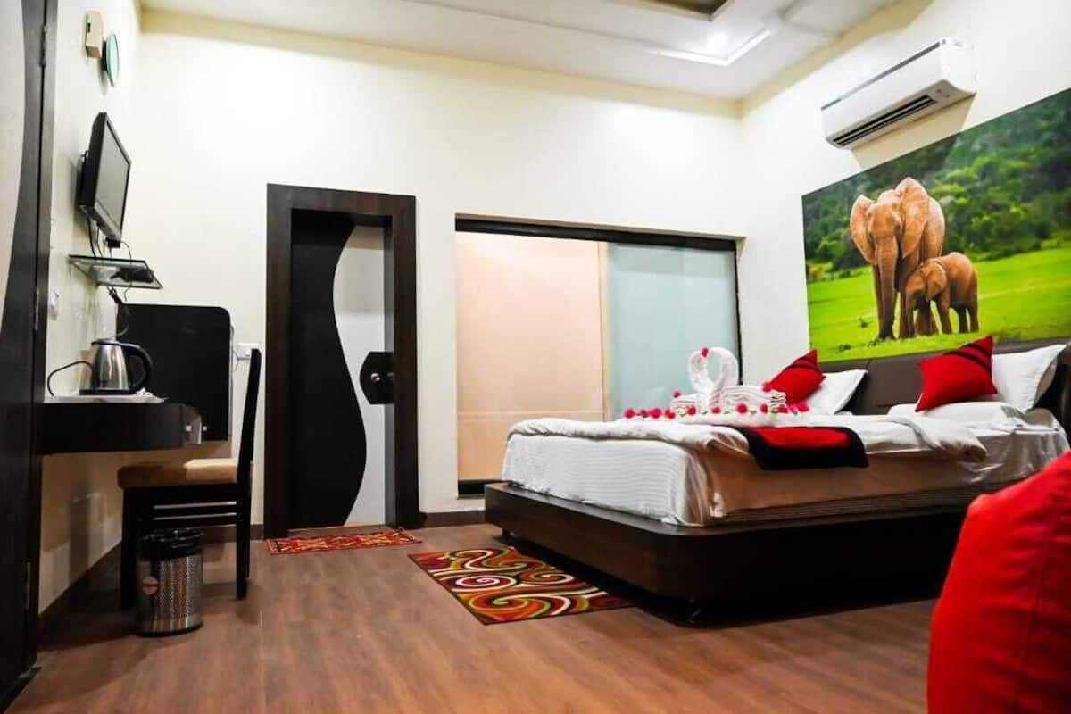 Habitación de hotel con cama, escritorio con computadora, silla, basurero, puerta y aire acondicionado instalado en la pared.