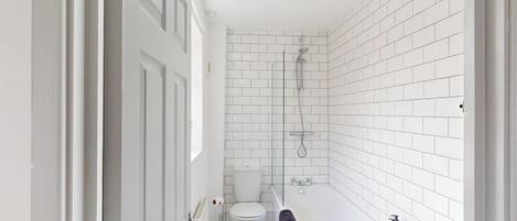 Un baño con paredes de azulejos blancos, un inodoro, una ducha y una bañera.
