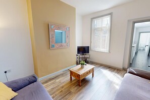 A living room with a sofa, a coffee table, a television on a stand, and a window with blinds. - Sunderland Cosy Cottage (Sunderland)