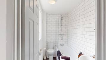 Um banheiro com paredes revestidas de azulejos brancos, vaso sanitário, banheira e chuveiro.