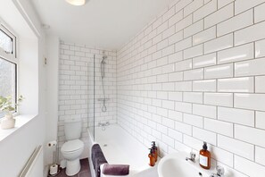 A bathroom with white subway tiles, a bathtub, a toilet, a sink, and a shower.
