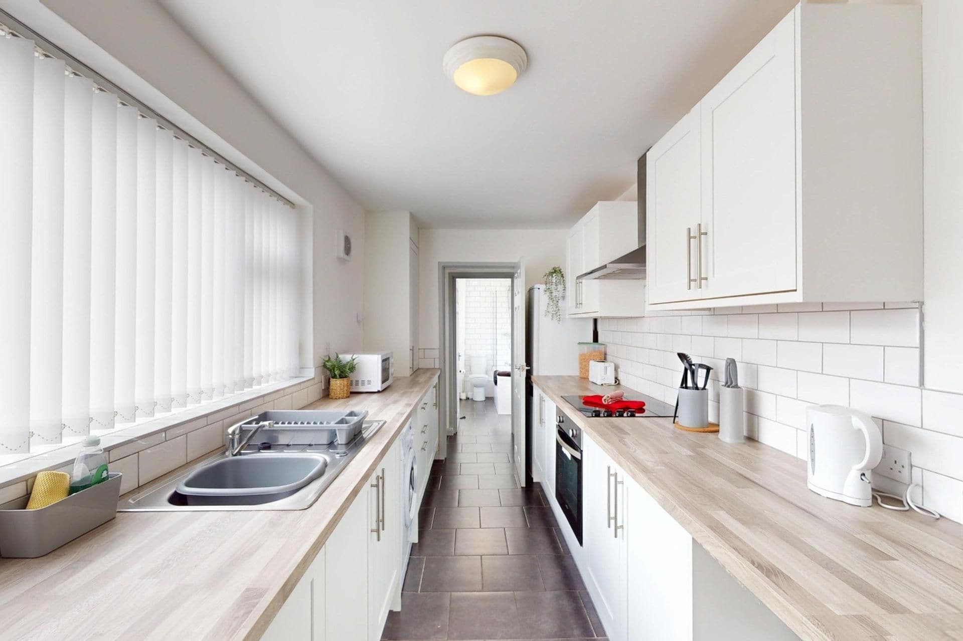 A modern kitchen with white cabinets, a wooden countertop, and a view into the adjacent bathroom.