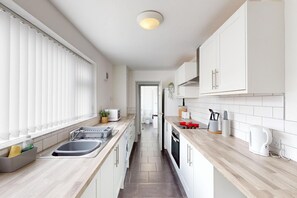 A modern kitchen with white cabinets, a wooden countertop, and a view into the adjacent bathroom. - Sunderland Cosy Cottage (Sunderland)