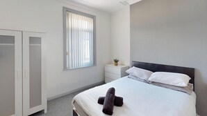 A bedroom with a bed, a nightstand, a window with blinds, a wardrobe, and a small plant on the nightstand. - Sunderland Cosy Cottage (Sunderland)