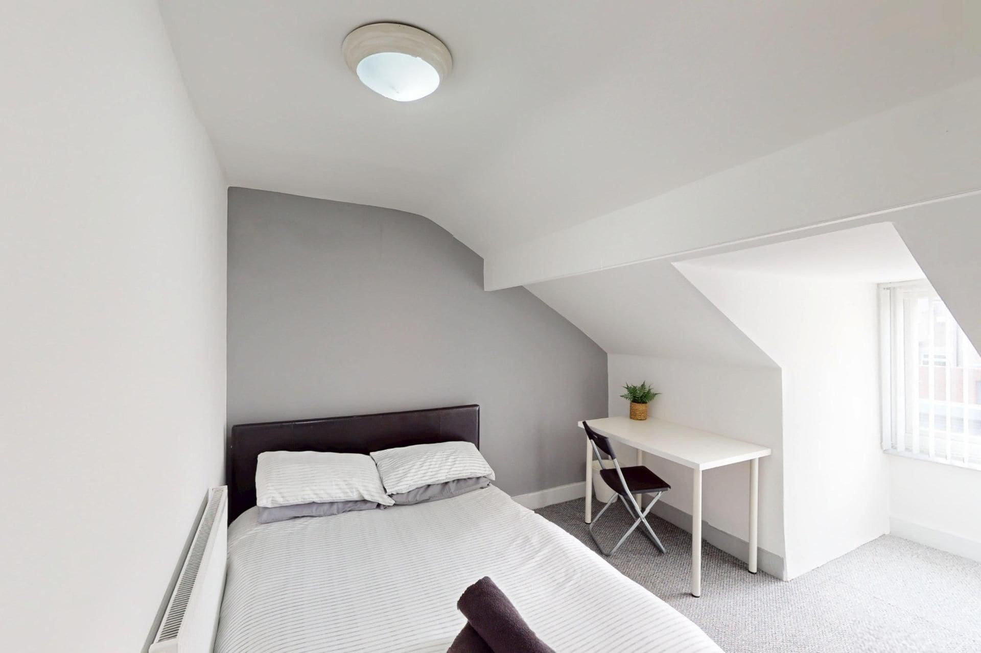 Ein modernes Schlafzimmer mit Bett, Schreibtisch und einer kleinen Pflanze.