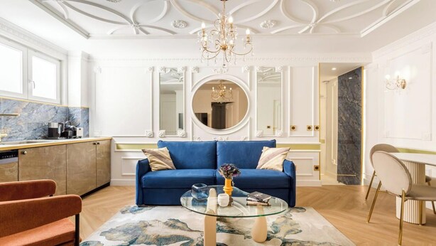 A modern living room with a blue sofa, a glass coffee table, and a red armchair.