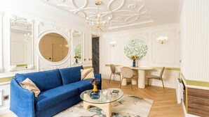 A living room with a blue sofa, a glass coffee table, and a dining area with a white table and chairs.