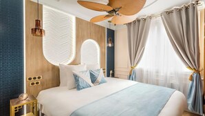 A modern hotel room with a large bed, a ceiling fan, and a large window with curtains.