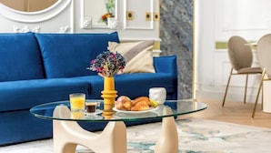 A modern living room with a blue sofa, a glass coffee table with breakfast items, and a decorative vase.