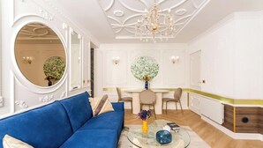 A modern living room with a blue sofa, a glass coffee table, and a chandelier.