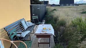 Een houten terras met een eettafel, een bank en een stoel.