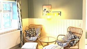 Een kamer met twee rieten stoelen, een tafeltje, een raam met gordijnen en een wandlamp.