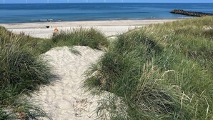 Een strand met een heldere lucht, zandstrand en windmolens in de verte.