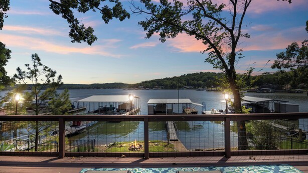 A lakeside deck with a fire pit, outdoor seating, and a view of the lake and dock area. - Pet-Friendly Lakefront Home in a Quiet Cove w/ Netflix, Outdoor Seating, Boat Slip (Climax Springs)