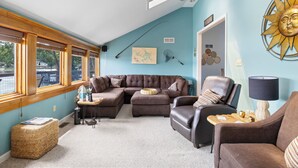 A living room with a sectional sofa, a leather armchair, a small table, and a lamp. There is a window with blinds, a ceiling fan, and a wall with a sun decoration. - Pet-Friendly Lakefront Home in a Quiet Cove w/ Netflix, Outdoor Seating, Boat Slip (Climax Springs)