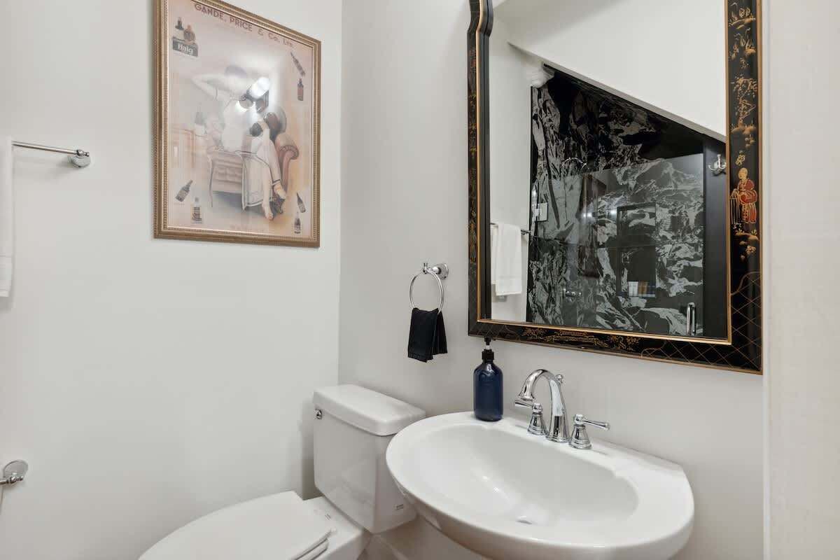A bathroom with a white sink, a toilet, a framed picture on the wall, and a mirror with a black frame.