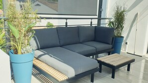 Ein moderner Sitzbereich im Freien mit einer grauen Couch, einem Couchtisch aus Holzlamellen und Topfpflanzen.