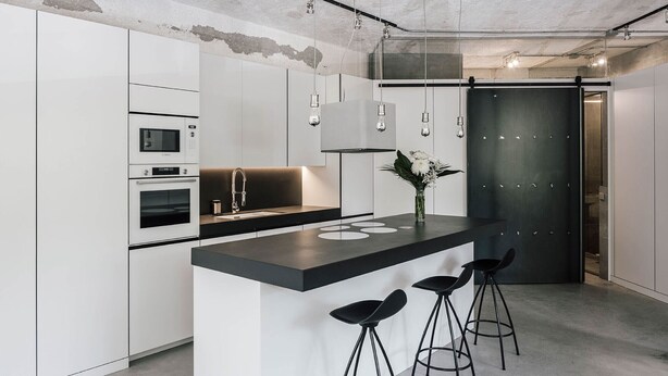 Une cuisine moderne avec des meubles blancs, un comptoir noir et trois tabourets de bar noirs.