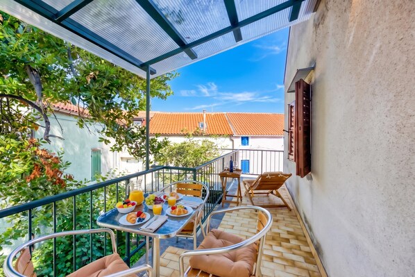 A balcony with a table set for breakfast, including fruits, pastries, and a glass of orange juice.