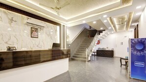 A hotel reception area with a marble reception desk, a staircase, and a wall-mounted refrigerator. - Hotel Devrana (New Delhi)