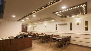 A spacious restaurant with multiple dining tables and chairs, a wooden counter, and modern lighting fixtures. - Hotel Devrana (New Delhi)