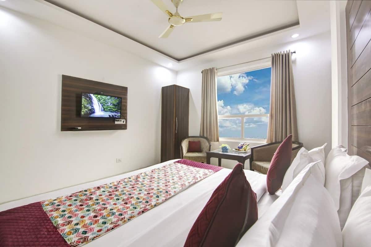 A hotel room with a bed, a television mounted on the wall, a window with curtains, and a ceiling fan.