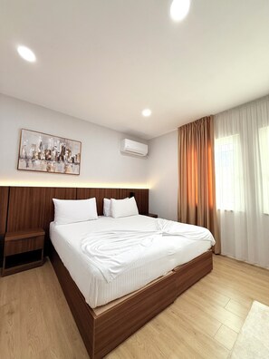 A hotel room with a wooden bed frame, a headboard, a bedside table, a wall-mounted air conditioner, and a painting. - Hotel Aleks (Shkodër)