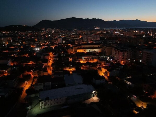 A nighttime cityscape with illuminated buildings and a mountain in the background. - Hotel Aleks (Shkodër)