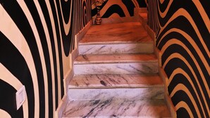Una escalera con un diseño de pared a rayas de cebra y un jarrón con flores en la parte superior.
