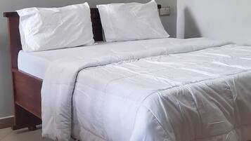 A neatly made bed with white bedding and a wooden headboard, a small red rug on the floor, and a wall-mounted light fixture.