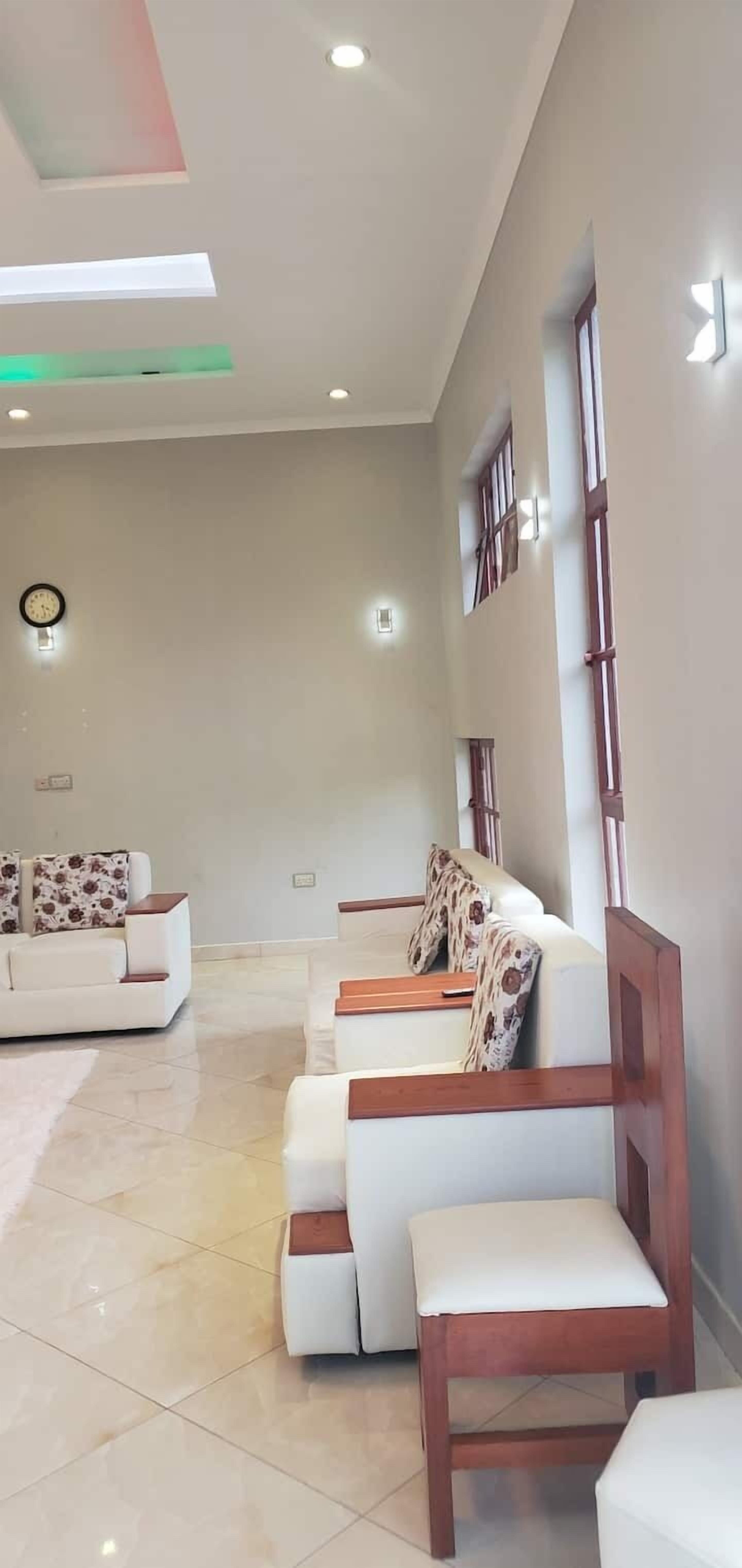 A modern interior with a sofa and chairs, a clock, and recessed ceiling lights.