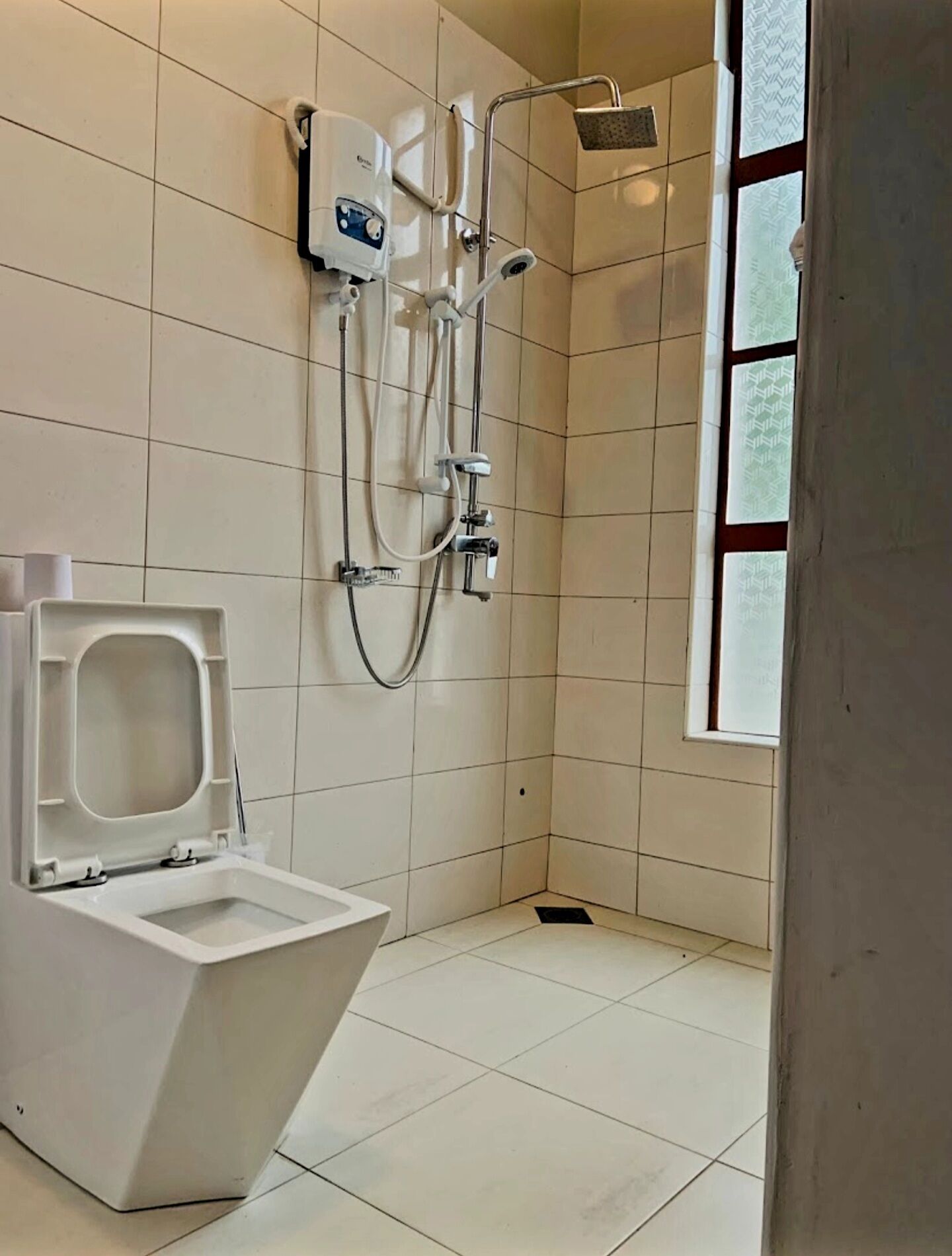 A bathroom with a toilet, a shower, and a window.