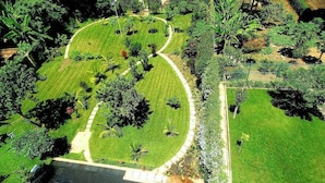 Vue aérienne d’un jardin bien entretenu, avec une pelouse centrale, entouré de divers arbres et arbustes.