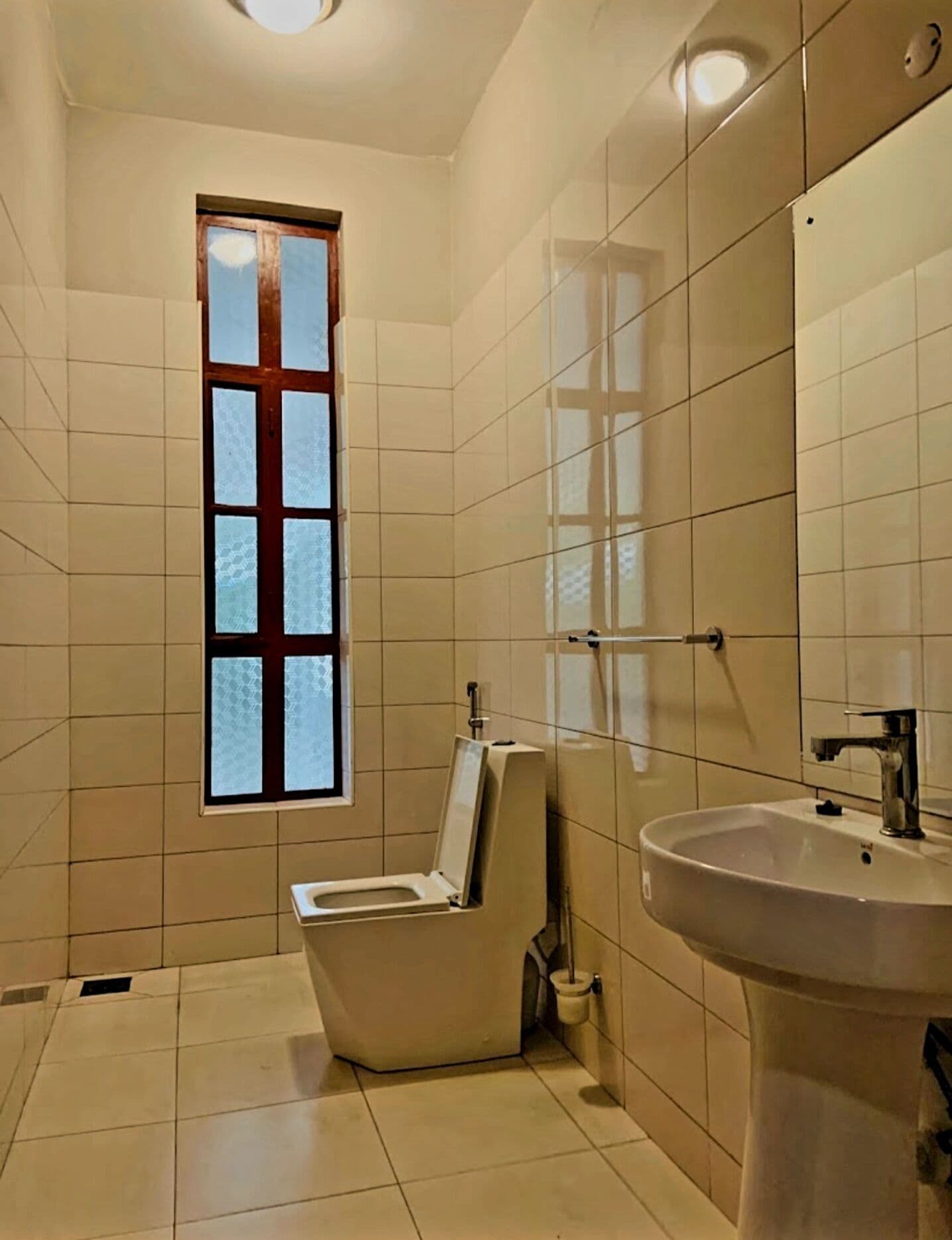 A small, tiled bathroom with a toilet, sink, and a window.