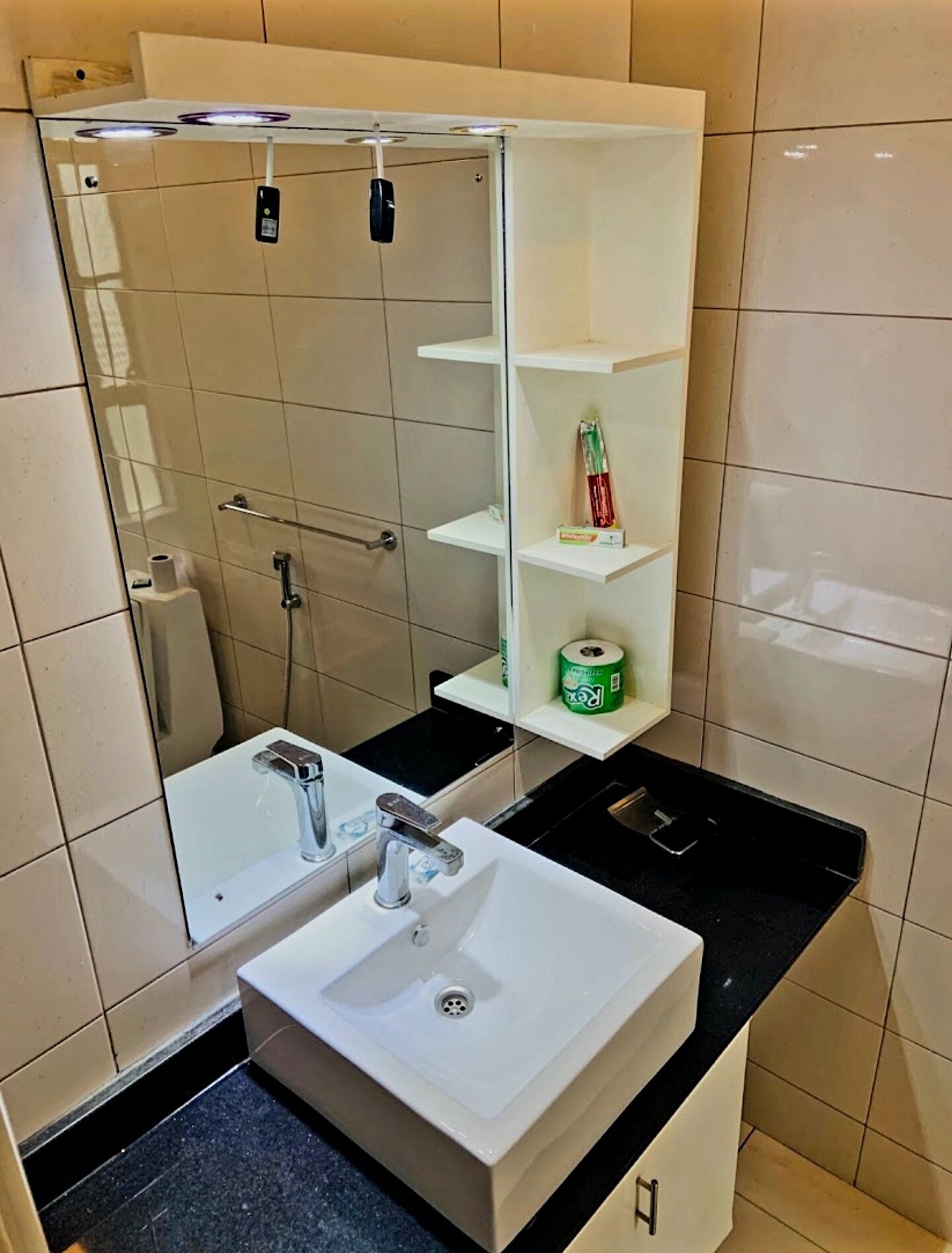 A modern bathroom with a glass-enclosed shower, a white sink, and a small shelf with toiletries.