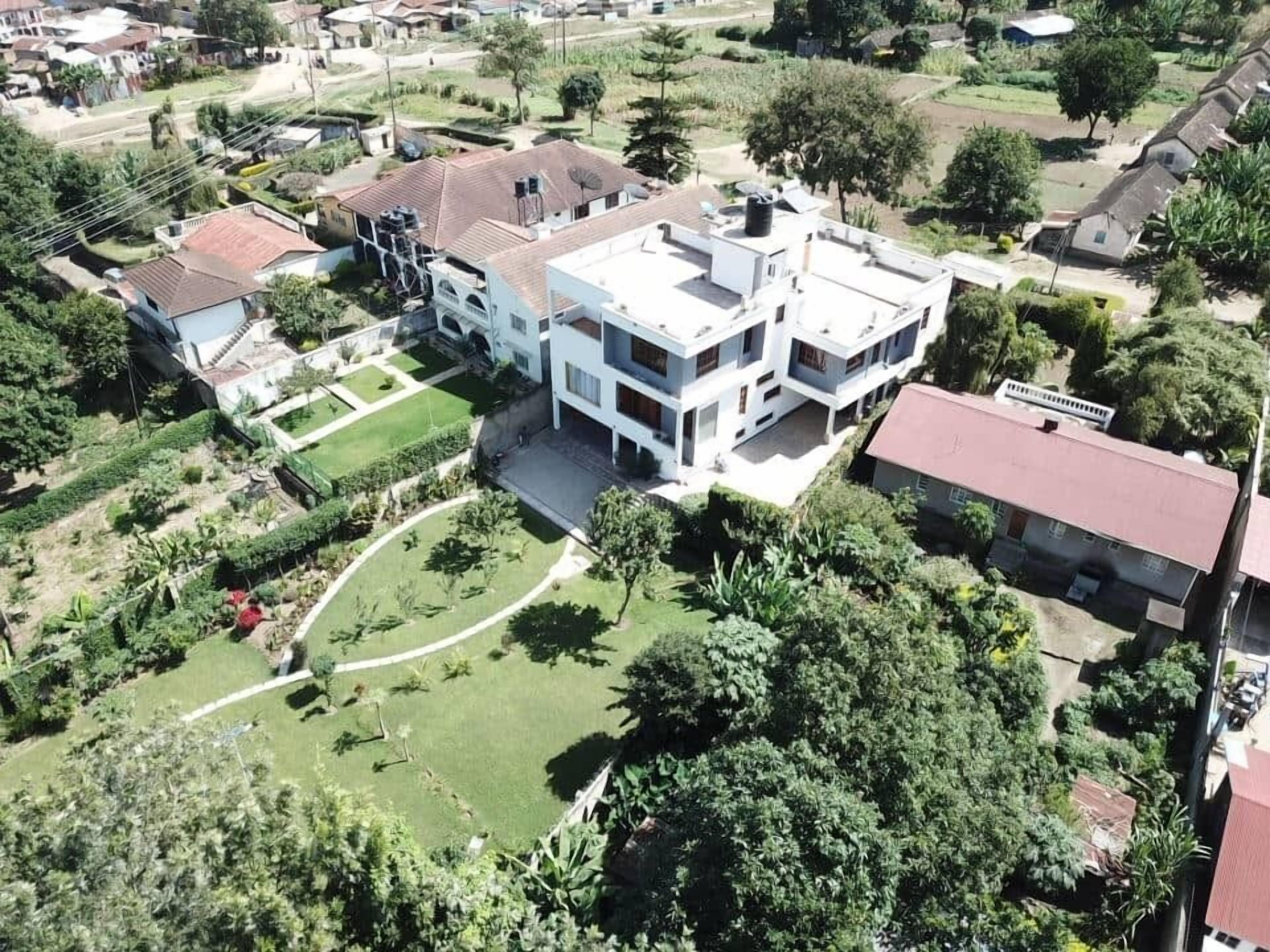 A modern multi-story residential building with a flat roof, surrounded by well-maintained gardens and trees.
