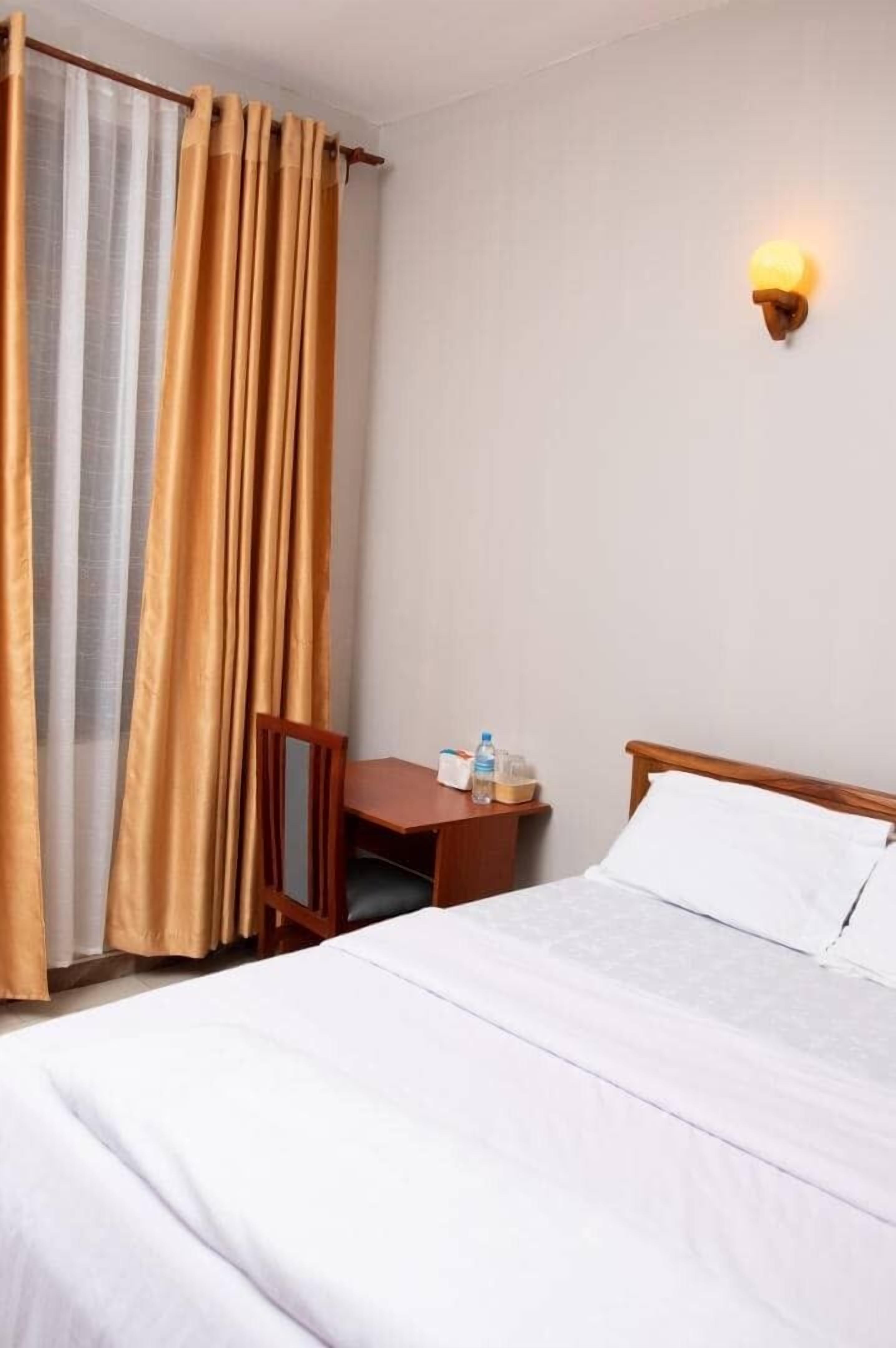 Una habitación de hotel con una cama, una mesita de noche, una mesa y una lámpara fijada a la pared.