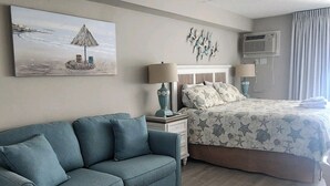 Een slaapkamer met een bed, een slaapbank, een nachtkastje, een lamp en een wandairconditioner.