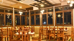 En restaurant med træborde og stole, store vinduer og hængende lamper.