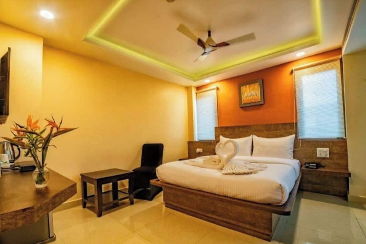 Ein Hotelzimmer mit Bett, Nachttisch, Stuhl und Schreibtisch mit Blumenvase.