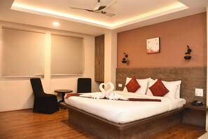 A hotel room with a large bed, a desk, a chair, and a window with blinds. - The Padma  (Imphal)