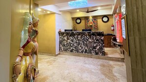 En hotellobby med marmorgulv, receptionsdisk, lysekrone og statue.