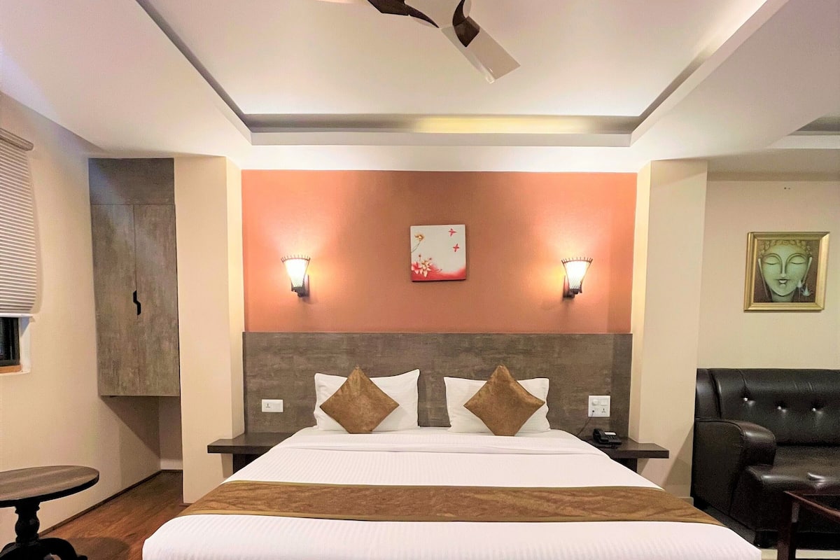 Ein Hotelzimmer mit einem großen Bett, einem Deckenventilator, zwei Wandleuchten, einem dekorativen Wandbild und einem schwarzen Leder Sofa.