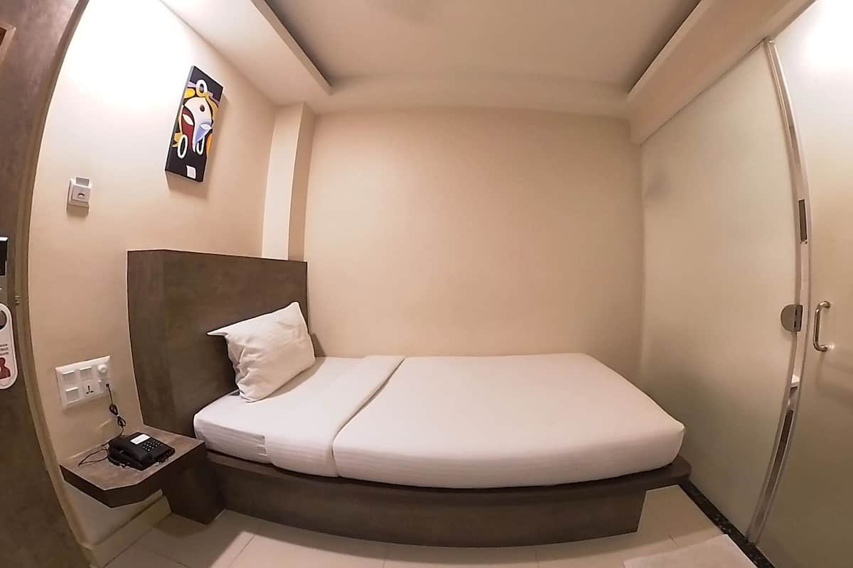 Ein kleines Hotelzimmer mit einem Einzelbett, einem Nachttisch mit Telefon und einem an der Wand hängenden Kunstwerk.