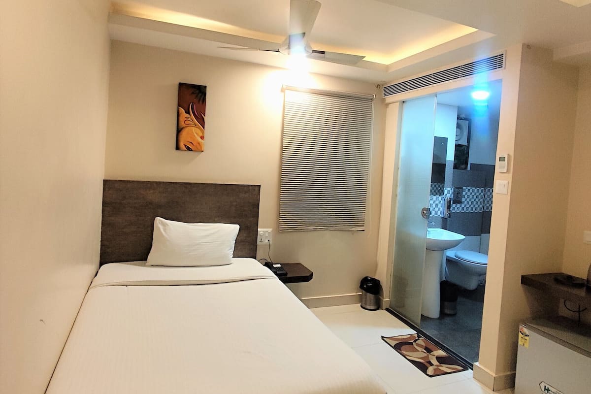 Ein Hotelzimmer mit einem Bett, einem Nachttisch, einem Deckenventilator, einem Fenster mit Jalousien und Blick ins Bad.