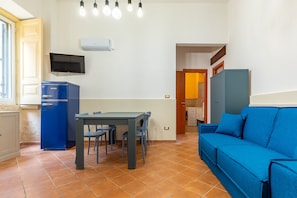 A compact living space with a dining area, a blue sofa, a television, and a small refrigerator.