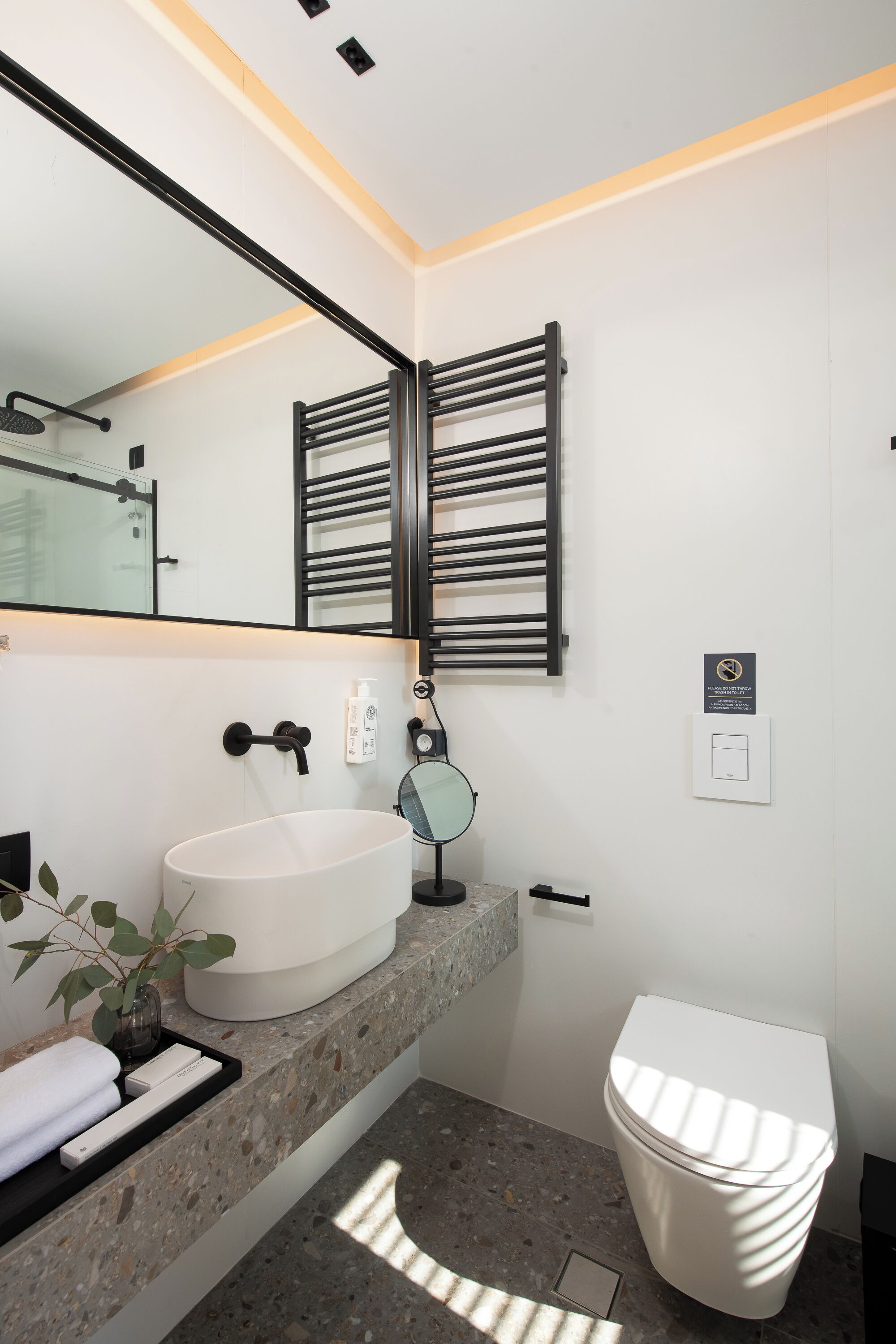 Un baño moderno con un lavamanos blanco, un perchero, un inodoro y un espejo.