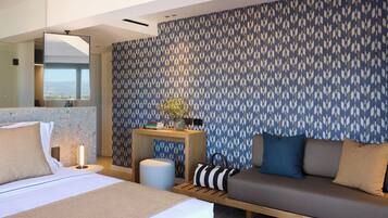 A modern hotel room with a large bed, a sofa, a small table with a lamp, and a patterned wall.