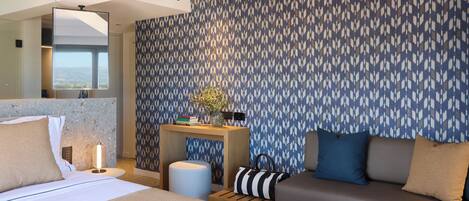 Una habitación de hotel moderna con una cama grande, un sofá, una mesita con una lámpara y un papel tapiz estampado.